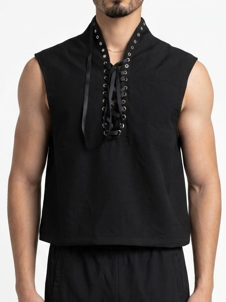 A man wearing a sleeveless black top with a high collar and front lace-up detail, photographed against a plain light background. Front view of black sleeveless lace-up top with metal eyelets, satin lacing, and high neckline.