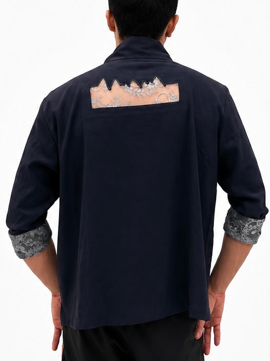 A man viewed from the back wearing a dark navy blue shirt with a decorative beige and silver mountain-patterned patch on the upper back and patterned gray cuffs. Back view of navy oversized overshirt featuring a floral lace back panel with scalloped edge detailing.