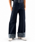 wide‑leg dark denim pants with patterned cuffs and high‑waist fit. Mo Kanani wide‑leg jeans with floral cuff detail styled on model